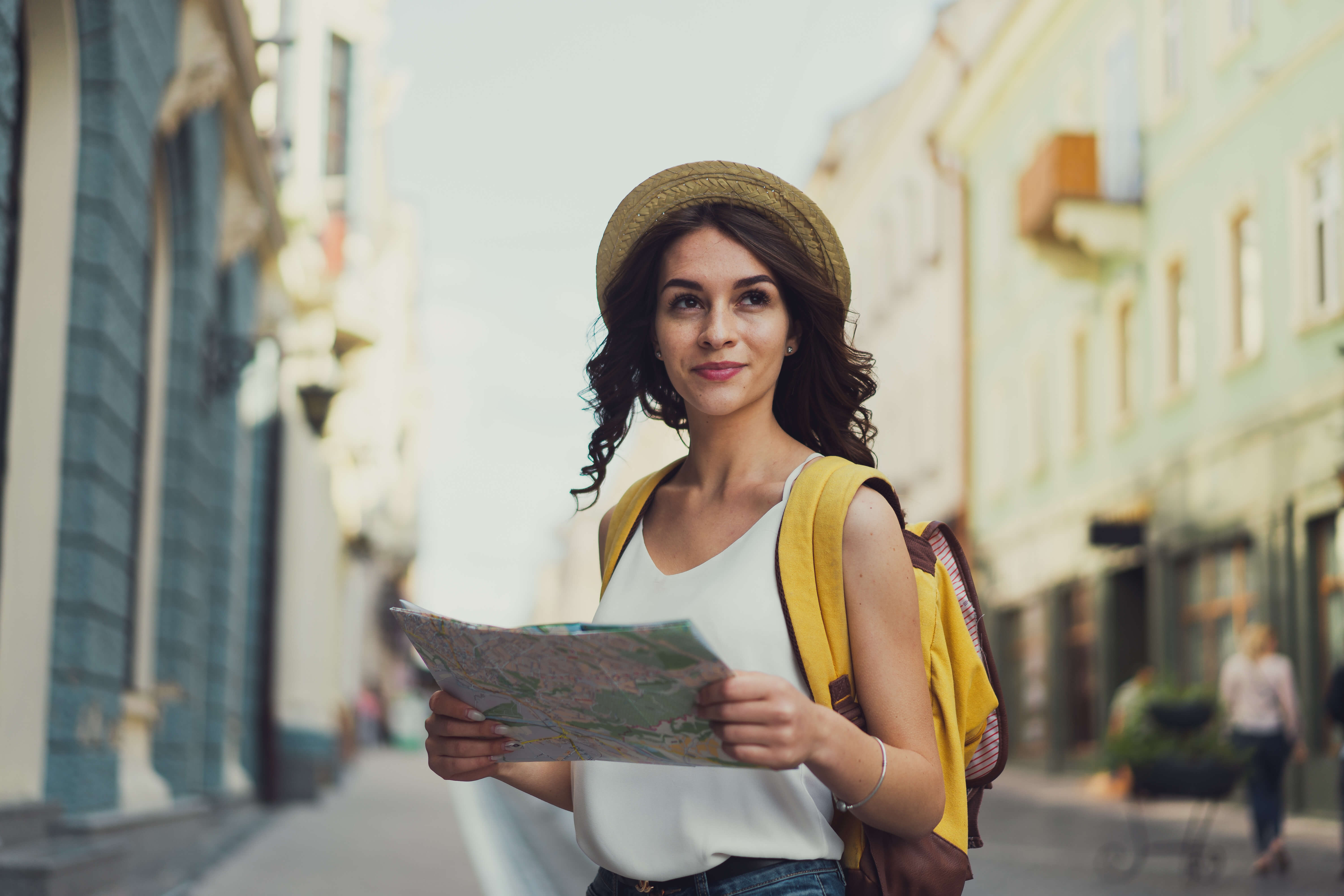 Young adult woman wearing hat and backpack holds a map in an international location.