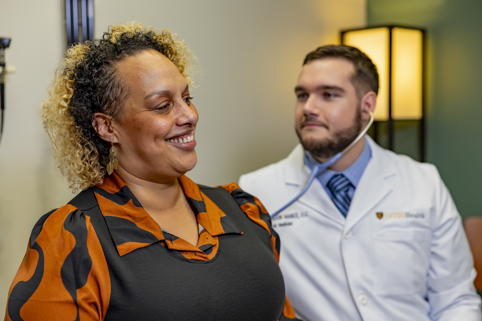 A doctor in a white coat listens to a woman's heartbeat using a stethoscope. 