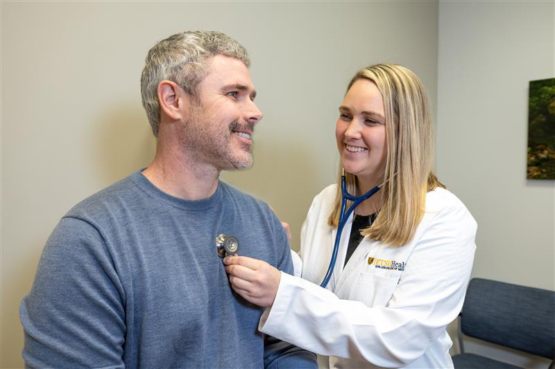 Resident doctor in a white coat listens to patient's heart with stethoscope.