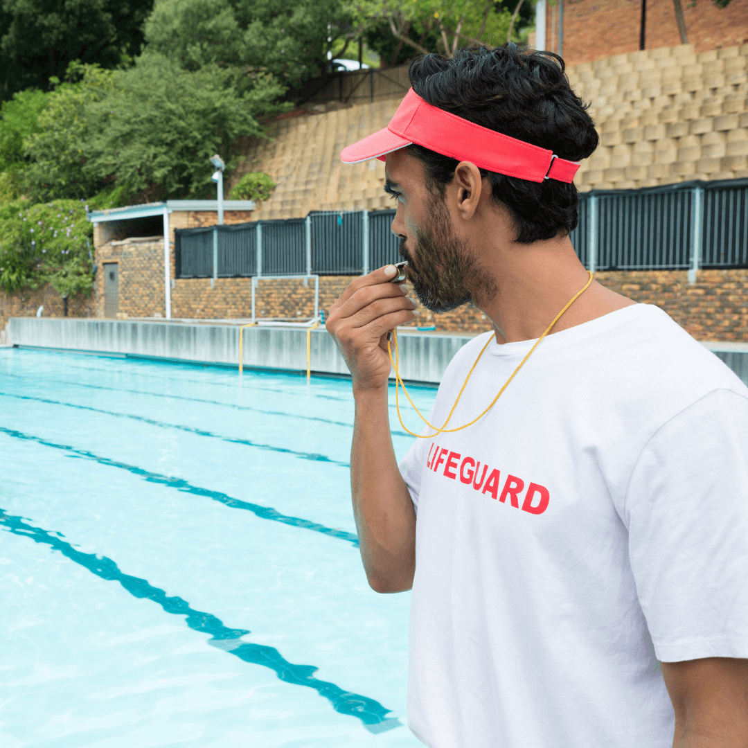 A male lifeguard on duty blowing the whistle for water safety concerns.