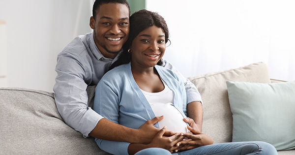 Pregnant person with partner smiling at the camera. 